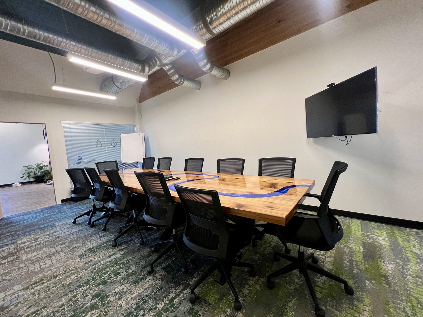 The boardroom: a live-edge wood table with a blue river inlay, twelve chairs and a wall-mounted screen